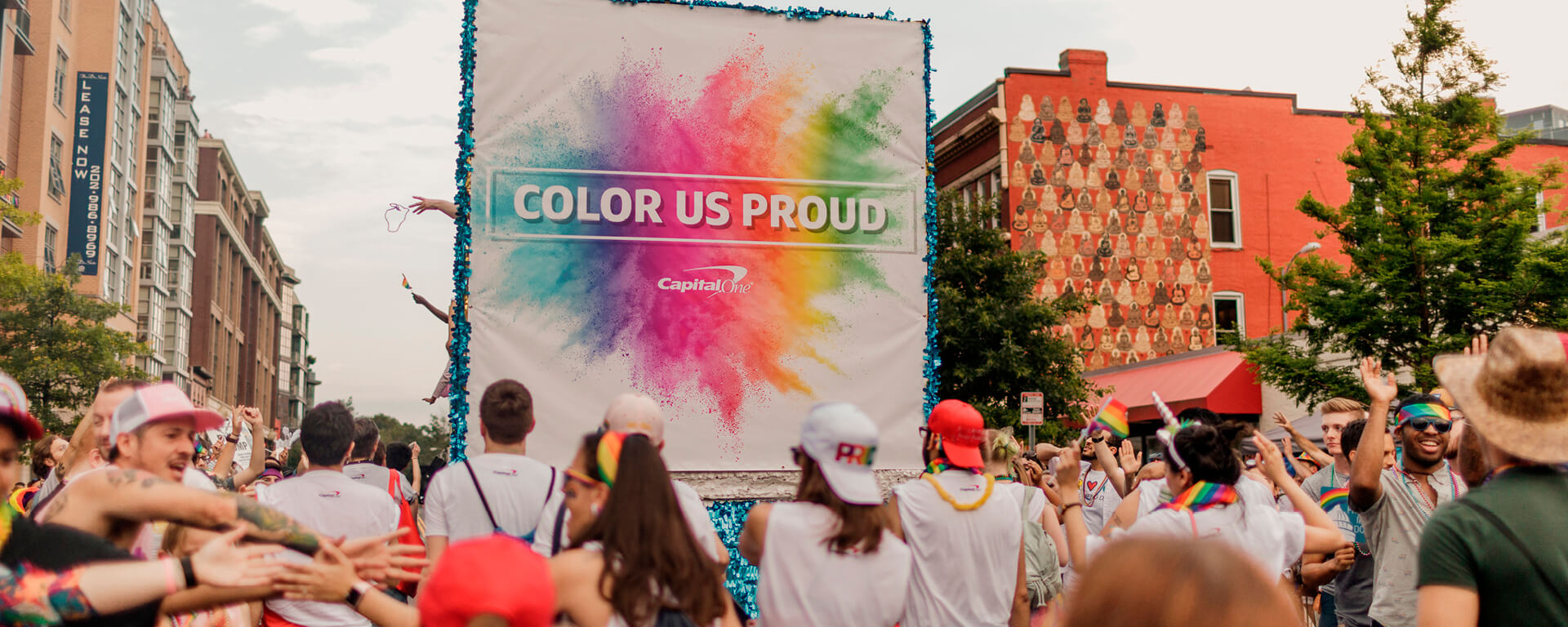 Capital One associates stand outside in a crowd celebrating Pride month with a large colorful banner that says 